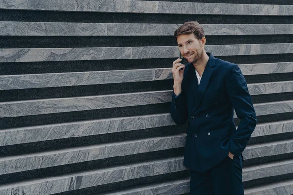 Trabalhador corporativo masculino vestido em terno preto formal mantém mão no bolso tem conversa telefônica — Fotografia de Stock