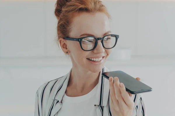 Porträtt av glad glad glad rödhårig kvinna i glasögon som håller mobiltelefon, inspelning ljudmeddelande — Stockfoto