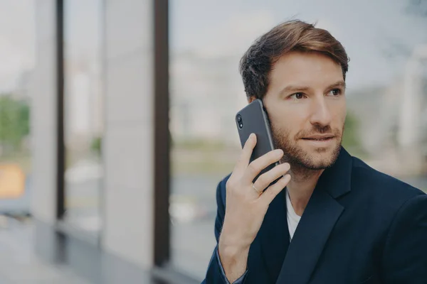 Empreendedor masculino pensativo focado na distância faz atender chamada usa telefone celular — Fotografia de Stock