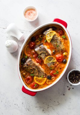 Balık bifteği, zeytin ve domates, domates sosu, kırmızı pişirilmiş trayon grisi arka planda. Düz yatıyordu