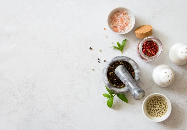 Seasonings- white, black and pink peppers, pink salt and shaker on gray stone background close up.Flat lay. Copy space