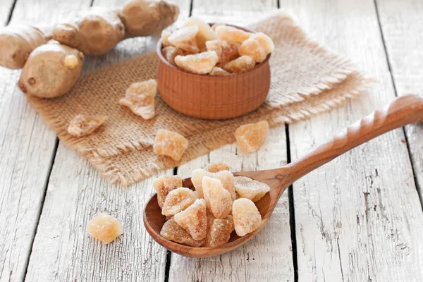 Raíz fresca de jengibre, trozos de caramelo de jengibre en una mesa de madera —  Fotos de Stock