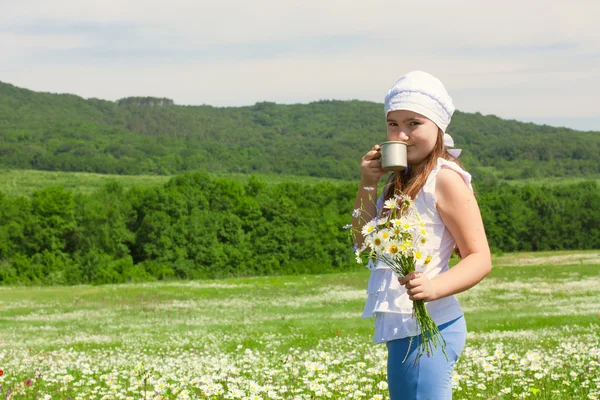 Enfant fille avec des fleurs et un verre de lait sur la prairie — Photo