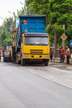 Melitopol, Ukrayna, tarih 27 Mayıs 2017. Yol işçileri kamyonu kontrol ediyor, asfalt kaldırımın arkasına boşaltılıyor, caddede yol onarımı yapılıyor.