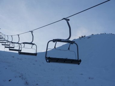 Üzerinde birkaç sandalye olan bir kayak asansörü. Sandalyeler karlı bir tepede. Gökyüzü mavi ve kar bembeyaz