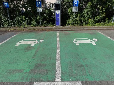 İki elektrikli araba şarj istasyonu olan bir otopark. Park yeri yeşil ve parkmetresi var.