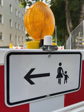 Üzerinde kadın ve çocuk olan bir imza ve solu gösteren bir ok. İşaret sarı ve siyah.