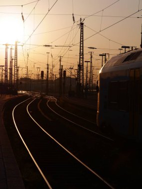 Tren arka planda günbatımı olan bir pistte ilerliyor. Tren görüntünün ana odak noktasıdır ve günbatımı sahneye sıcak ve huzurlu bir atmosfer ekler.