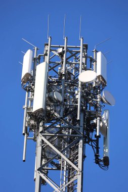 Telekomünikasyon kulesine yakın çekim, açık mavi gökyüzüne kurulmuş anten ve kablolar, modern teknoloji ve bağlantıyı temsil ediyor..
