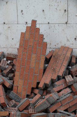 Kırık ve çökmüş kırmızı tuğlalardan oluşan bir hava manzarası ve gri harç kullanılmış, açık renkli ahşap ya da beton bir yüzey üzerinde duruyor. Olay yeri hasar ve yıkımı gösteriyor..