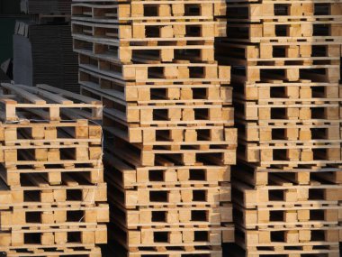 Aralarında bir sürü boş alan olan bir yığın ahşap palet. Paletler üst üste istiflenmiş, bazıları diğerlerinden daha uzun.