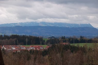Uzakta bir dağ sırası görülebilir, ön planda bir kasaba vardır. Gökyüzü bulutlu, ortama kasvetli bir hava katıyor.