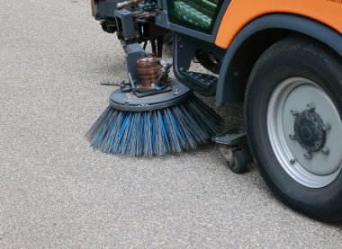 Sokak temizleyicisi mavi bir fırçayla caddeyi temizliyor. Fırça kamyonun arkasına bağlı.