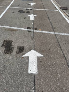 Gri asfalt bir yüzeye boyanmış üç beyaz ok yönü gösteriyor. Asfalt bazı aşınmalar, çatlaklar ve koyu lekeler gösteriyor, muhtemelen yağ ya da sudan. Kempten 'de