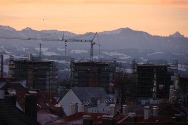 A view of a construction site during sunset, featuring scaffolding and mountains in the background. A blend of urban and natural scenery.