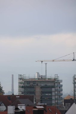 Crane büyük bir binayı kaldırıyor. Gökyüzü bulutlu ve bina evlerle çevrili.. .