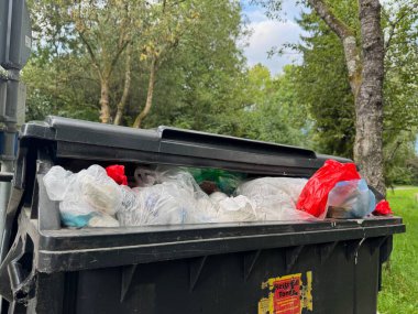 Çöp kutusu plastik torbalar ve şişelerle dolu. Çöp tenekesi bir parkta.