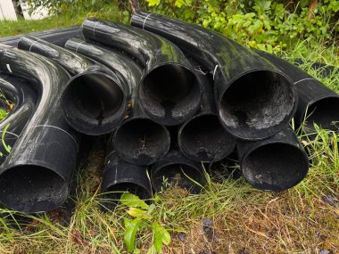 Yere siyah borular yığıldı. Borular siyah ve parlak bir yüzeyi var. Sanayi veya inşaat işi kavramı