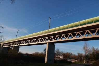 Yeşil korkuluklu ve arkasında mavi gökyüzü olan bir köprü. Köprü uzun ve nehir boyunca uzanıyor.