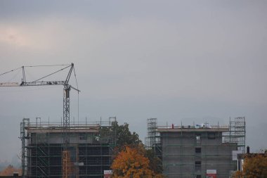 İnşaat alanında vinç ve iskele var. Gökyüzü bulutlu ve binalar yapım aşamasında. .