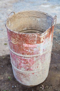 Çok renkli lekelerle kaplı eski paslı metal bir fıçı sokakta duruyor. Tamir ve inşaat için her şeyi.