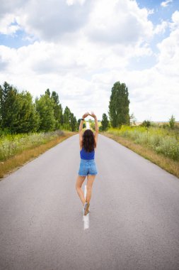 Çekici kız, poz veriyor, ellerini kaldırıyor, alanın yakınındaki asfalt yolun ortasında, içerik alanı kopyalıyor..