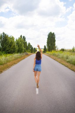 Çekici kız, poz veriyor, ellerini kaldırıyor, alanın yakınındaki asfalt yolun ortasında, içerik alanı kopyalıyor..