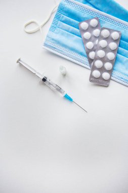 Covid-19 'a karşı aşı hazırlığı. Şırınga, aşı, haplar, beyaz bir masada tıbbi maske. Yukarıdan görüntüle