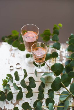Okaliptüs dalları eski bir masanın üzerinde bir bardak gül şarabı ve alyansla