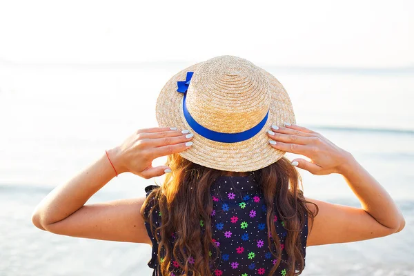 stock image Beautiful girl in a hat stands with her back on a sandy beach.