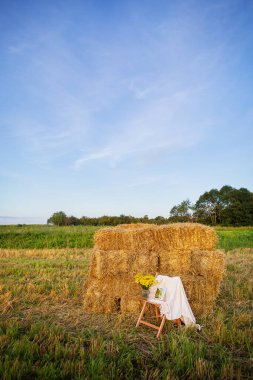 Tarlada saman balyalarının yanında piknik. Batan güneş. Köy tarzı. Ahşap sandalye, ekose, çiçek buketi, ayna. Romantik randevu