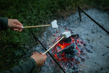 Marşmelovlar ateşte kızartılır. Kızarmış marşmelov ve şişte açık alev. Kamp ateşi romantizmi, yaz akşamı