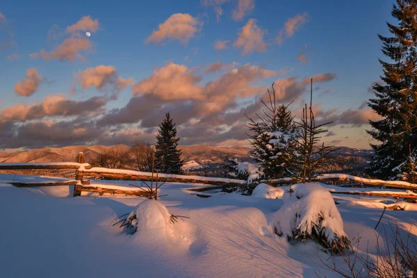 最後の夜の日没の太陽の光でアルパイン村の郊外 冬の雪の丘やモミの木 — ストック写真