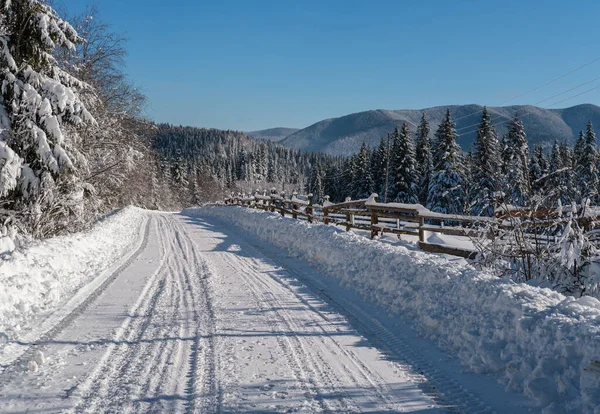 道端に雪のモミの森 雪のドリフトや木のフェンスを介してリモート山の集落への2番目の田舎の高山道路 — ストック写真