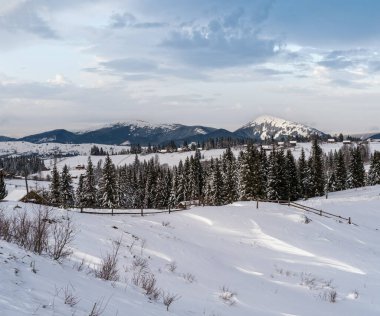 Kışın uzak dağlık dağlık köyde kırsal tepeler, ağaçlar ve tarım arazileri.