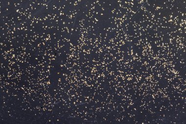 Closeup view of gold flakes collected in a black panning pan. Shiny metallic particles representing mining, prospecting, natural resources, and the search for wealth and treasure.
