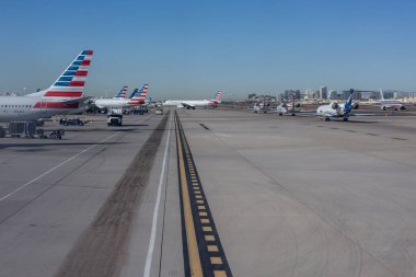 PHOENIX, ARIZONA, ABD, NOVEMBER 09, 2025: Phoenix Sky Harbor Uluslararası Havalimanı 'ndaki (PHX) pistin bir uçak penceresinden havalimanı binaları ve çöl dağları olan kapılarda parketmiş çok sayıda Amerikan Hava Yolları uçağı görülüyor