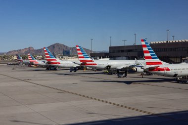 PHOENIX, ARIZONA, ABD, NOVEMBER 09, 2025: Phoenix Sky Harbor Uluslararası Havalimanı 'nın (PHX) terminal kapısında parkedilmiş çoklu Amerikan Hava Yolları uçakları ve köprüleri ve çöl dağlarını gösteren bir manzara 