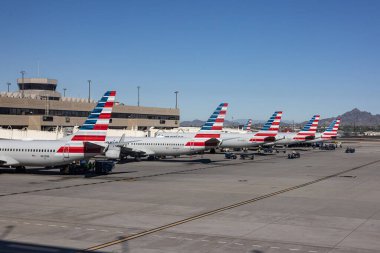 PHOENIX, ARIZONA, ABD, NOVEMBER 09, 2025: Phoenix Sky Harbor Uluslararası Havalimanı 'nın (PHX) terminal kapısında parkedilmiş çoklu Amerikan Hava Yolları uçakları ve köprüleri ve çöl dağlarını gösteren bir manzara 