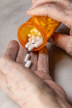 Turuncu bir ilaç şişesinin içinden çekilen güçlü bir birinci şahıs POV, beyaz ve sarı haplar yaşlı ve buruşuk bir ele dağılıyor..