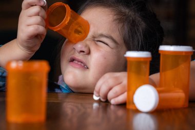 Reçetesiz ilaç ya da şişelere uzanan genç bir kızın (anaokulu çocuğu) masumiyetini ve merakını gösteren yakın plan bir fotoğraf..