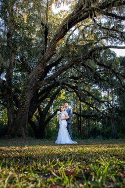 Güzel bir çiftin (gelin ve damat) İspanyol yosunlarıyla büyük meşe ağaçlarının altında evliliklerini kutlayan samimi ve zarif bir düğün portresi..