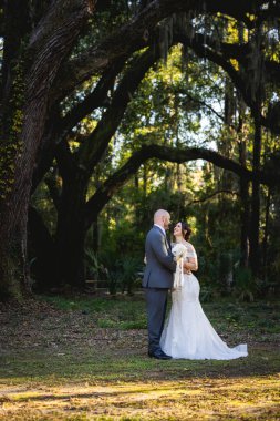 Güzel bir çiftin (gelin ve damat) İspanyol yosunlarıyla büyük meşe ağaçlarının altında evliliklerini kutlayan samimi ve zarif bir düğün portresi..