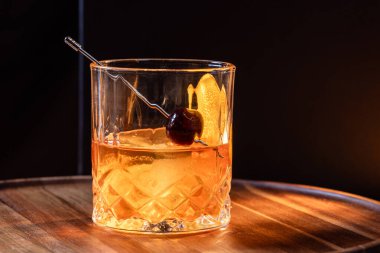 Kayalarda servis edilen viski kokteyli portakal kabuğu ve kirazla süslenmiş ve ahşap bir yüzeyde sunulan dramatik ışıklandırmayla servis ediliyor..