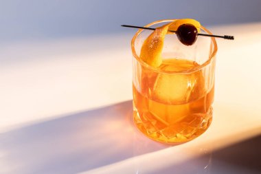 Manhattan kokteyline yakın bir yerde yansıtıcı beyaz bir yüzey üzerinde büyük bir buz küpü ile servis edilir. İkili aydınlatma tonları ve yüksek kontrastlı ışıklar dram katar..