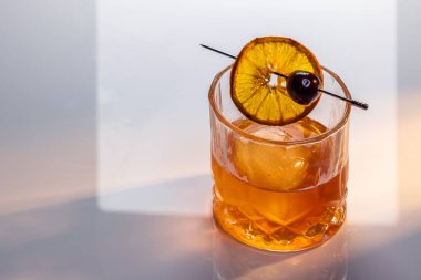 Manhattan kokteyline yakın bir yerde yansıtıcı beyaz bir yüzey üzerinde büyük bir buz küpü ile servis edilir. İkili aydınlatma tonları ve yüksek kontrastlı ışıklar dram katar..