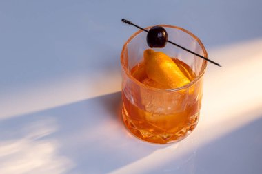 Manhattan kokteyline yakın bir yerde yansıtıcı beyaz bir yüzey üzerinde büyük bir buz küpü ile servis edilir. İkili aydınlatma tonları ve yüksek kontrastlı ışıklar dram katar..