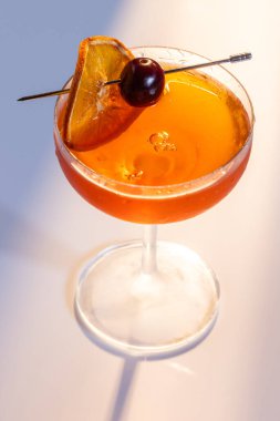 Güzel bir kehribar kokteyli, bir Negroni veya Manhattan dramatik ışıklandırmayla beyaz bir yüzey üzerinde servis edilir..