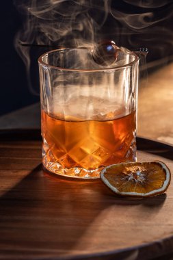 Kurutulmuş portakal dilimiyle süslenmiş buzlu viski kokteyli ve ahşap bir yüzey üzerinde çarpıcı ışıklandırmayla servis edilen kiraz..