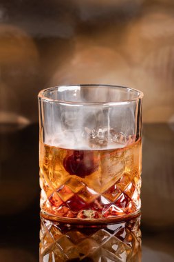 Kokteylin üstünde portakal kabuğu ve kirazla servis edilen aromatik duman. Dramatik ışıklandırma kullanımı, kokteylin dumanını ve hissini vurgular..